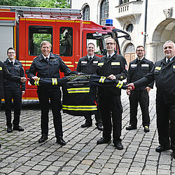 Gruppenbild mit Jacke: OBD Wolfgang Schäuble, die Kommandanten der FFM (v.l.) Florian Klein, Claudius Blank und Michael Schmid sen. Im Hintergrund (v.l.) Thomas Elser (persönlicher Mitarbeiter des Dienststellenleiters), Michael Buchner (stellv. Abteilungskommandant Abt. Stadtmitte und Beauftragter für die PSA-Kommissionierung) sowie Geschäftsführer Stefan Bründl. Foto: BF, Jan Saurer